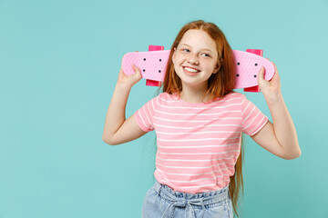 Little redhead kid girl 12-13 year old in pink striped t-shirt hold skateboard rest behind head neck enjoy leisure time isolated on pastel blue background studio. Children lifestyle childhood concept