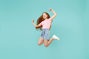 Full length little fun overjoyed redhead kid girl 12-13 year old in pink striped t-shirt do winner gesture clench fist isolated on pastel blue background studio Children lifestyle childhood concept.
