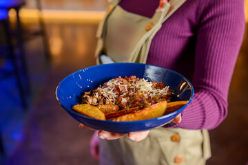 Roasted or baked potatoes with vegetable gravy in a blue bowl served by waiter in restaurant or diner.