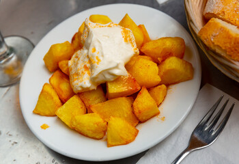 Spanish cuisine patatas bravas served with sauce on plate on wooden table