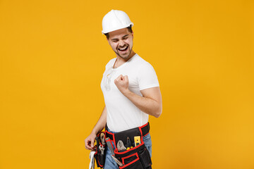 Young employee handyman man in protective helmet hardhat do win gesture clench fist scream yes isolated on yellow background Instruments accessories for renovation apartment room Repair home concept.
