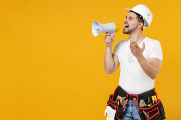 Young employee handyman man in protective helmet hardhat scream shout in megaphone spread hands isolated on yellow background. Instruments accessories renovation apartment room Repair home concept