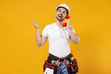 Young employee handyman man in protective helmet hardhat speak by handset phone spread hands isolated on yellow background studio Instruments accessories renovation apartment room Repair home concept.