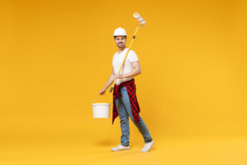 Full length fun young employee handyman man wear t-shirt holding paint roller look camera walk isolated on yellow background Instruments accessories for renovation apartment room. Repair home concept.