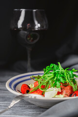 Salad with tomatoes and mozzarella topped with fresh arugula and a glass of red wine. Italian cuisine concept.
