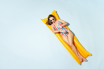 Top view young sexy woman slim body in striped one-piece swimsuit lies on inflatable mattress hotel...
