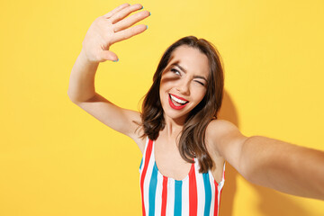 Fototapeta premium Close up happy fun young sexy woman slim body wear striped red blue one-piece swimsuit doing selfie shot isolated on vivid yellow color background studio. Summer hotel pool sea rest sun tan concept.