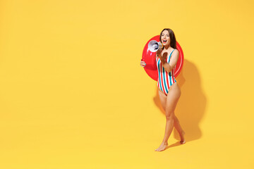 Full length happy sexy woman slim body wear red blue swimsuit hold inflatable rubber ring scream megaphone isolated on vivid yellow color background studio. Summer hotel pool sea rest sun tan concept