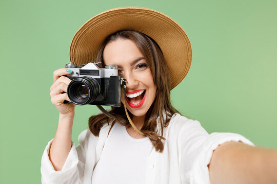 Traveler tourist woman in casual clothes hat taking selfie picture on retro photo camera cell phone isolated on green background Passenger travel abroad on weekends getaway Air flight journey concept