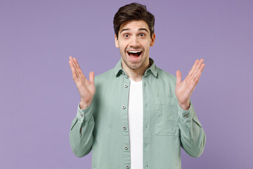 Fototapeta premium Young amazed surprised impressed fun caucasian man 20s years old wearing casual mint shirt white t-shirt spread hands isolated on purple violet background studio portrait. People lifestyle concept
