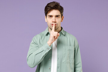 Young secret caucasian man 20s wearing mint shirt white t-shirt say hush be quiet with finger on lips shhh gesture look camera isolated on purple background studio portrait. People lifestyle concept