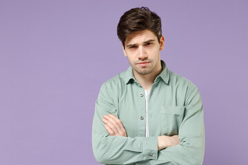 Young sad serious frowning european man 20s years old wearing casual mint shirt white t-shirt hold hands crossed folded isolated on purple violet background studio portrait. People lifestyle concept