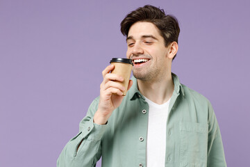 Young smiling satisfied fun man 20s in casual green mint shirt white t-shirt holding paper cup of coffee drink hot tea in morning sniff with closed eyes isolated on purple background studio portrait.
