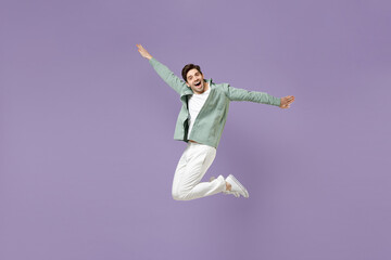 Fototapeta premium Full length excited overjoyed energetic cool young man in casual mint shirt white t-shirt jump high with outstretched hands look camera isolated on purple violet background. People lifestyle concept
