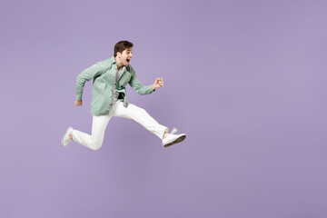 Fototapeta na wymiar Full length side view overjoyed amazed fun young man in casual mint shirt white t-shirt jump high running fast hurrying up look camera isolated on purple violet background. People lifestyle concept