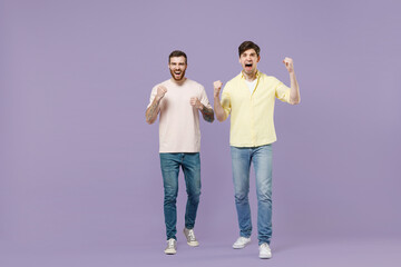 Fototapeta premium Full length overjoyed two young happy men friends together in casual t-shirt walking do winner gesture clench fist isolated on purple background studio portrait People friendship lifestyle concept
