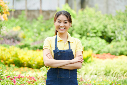 Smiling gardening center worker in denim apron crossing hands and looking at camera