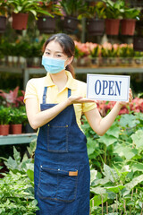 Lovely young woman wearing protective mask when inviting customers in gardening center