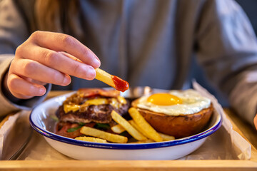 Close-up of French fries in ketchup in a woman's hand in a cafe.
