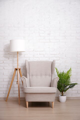 Armchair, lamp and plant with copy space over brick wall
