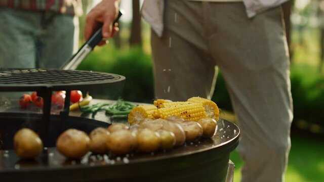 Male chef using forceps for cooking food outdoors. Man hands pouring salt on bbq