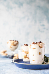 Traditional Italian dessert tiramisu in glass, light background. Coffee flavored portion dessert made of ladyfingers and mascarpone decorated with cocoa powder.