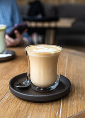Cappuccino with latte art in glass cup on wooden table in cafe or coffeehouse.