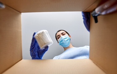 Fototapeta na wymiar home delivery, shipping and pandemic concept - woman in protective medical mask and gloves unpacking parcel box with cosmetics and beauty products