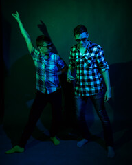 Two young men in plaid shirts dance in the studio with multicolored light