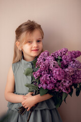 cute little girl with beautiful eyes and a bouquet of lilacs in a green dress with smiling and looking at the camera. monochrome background, congratulations, memory, respect. postcard.