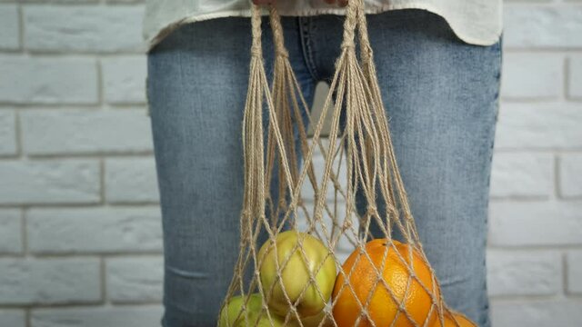Fruit bag in quarantine. A girl hold a string eco bag with apples and citrus in the room.