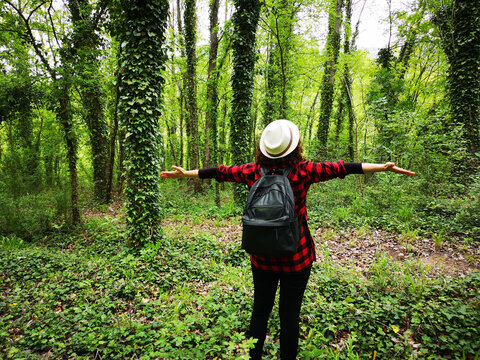Rear view of a woman with open arms looking at the trees covered with crawling vines in Italy
