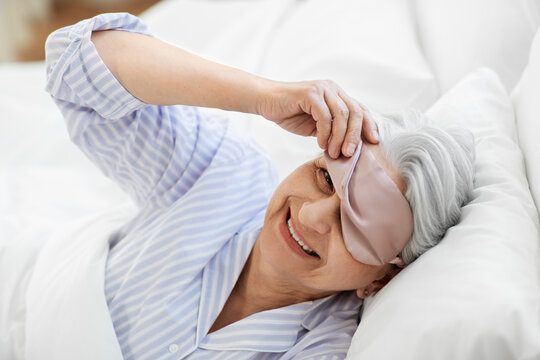 Old Age And People Concept - Happy Smiling Senior Woman With Eye Sleeping Mask In Bed At Home Bedroom