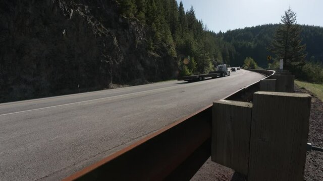 A guard rail stands between traffic streaming up a mountain highway and the valley below on this sunny spring morning on Highway 26 near Government Camp, OR at Silent Rock.  Extreme wide angle.