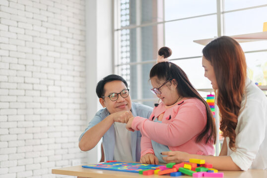 Happy asian father and mother playing education toy with their daughter down syndrome child in living room, Dad giving fist bump with daughter, Activity happy family lifestyle concept.