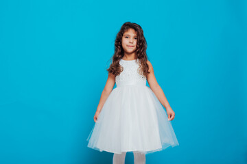 Naklejka premium Beautiful little curly girl 5 years old in a white dress on a blue background