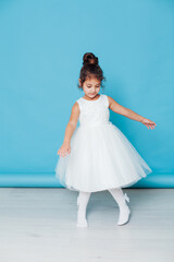Fototapeta na wymiar Beautiful little girl dances to the song in a white dress on a blue background