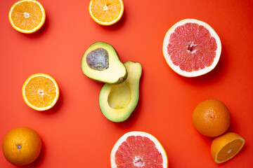 Composition of avocado, grapefruit and oranges some of them sliced over a red background