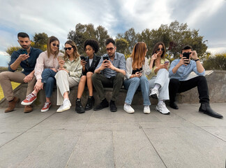 Diversity young people browsing social network content online sitting on a bench in the park