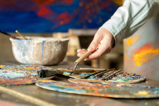 Woman artist hand takes a brush on a painting background. artist creates a painting in the studio