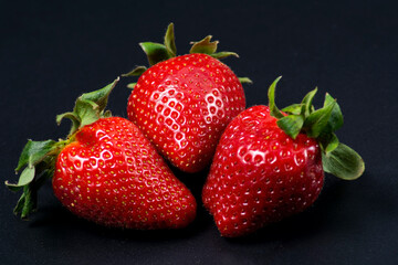 Three juicy large strawberries on a black background.