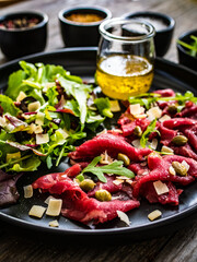 Beef carpaccio  with parmesan, capers, and arugula on wooden table
