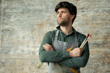 Portrait of a contented young male artist crossing his arms with a brush in his hand on a...