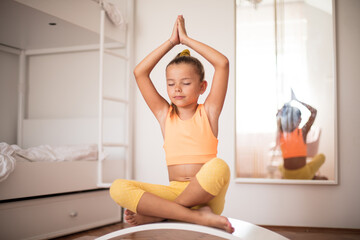 Little girl doing yoga exercise at home on board.