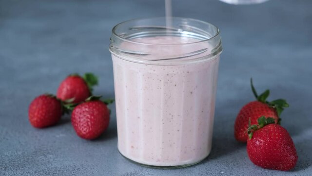 Pouring strawberry smoothie in jar. Thick protein strawberry milkshake poured in a drinking jar