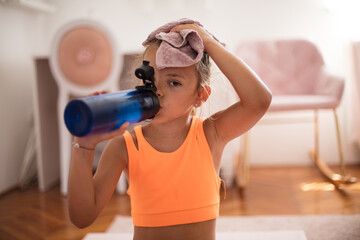 Little girl drinking water after exercise and cleaning sweat with towel. - obrazy, fototapety, plakaty