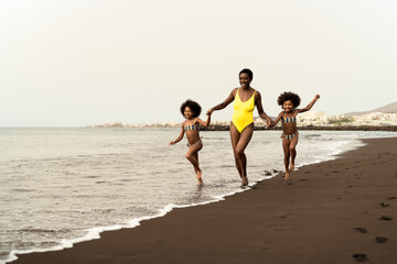 Happy Afro family having fun running on the beach during summer time - Parents love and travel lifestyle concept