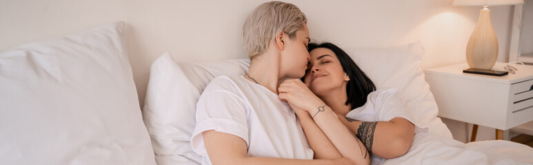 young lesbian couple lying in bed and holding hands, banner