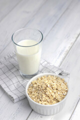 Alternative milk for vegetarians and vegans. Oatmeal, vegetable milk in a glass and oat flakes near on a white wooden background. Vertical photo.