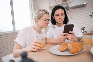 Obraz na płótnie Canvas brunette woman using smartphone near girlfriend in kitchen